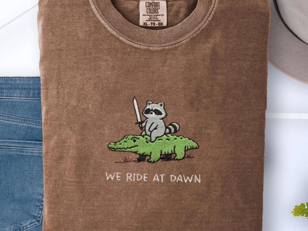 We Ride At Dawn Embroidered Comfort Colors T-Shirt: Raccoon Riding Alligator with Sword - Funny Fantasy Meme Animal Tee Gift for Gamers